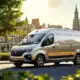 Сучасний електричний комерційний автомобіль Ван ден Хурка в міському середовищі, оточений зеленню, символізує стійкість та інновації.