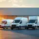 Three modern electric commercial vehicles in different sizes parked on car dealership lot with glass showroom