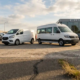 Witte bestelbus en grote personenminibus naast elkaar op zonnig dealerterrein, grootteverschil benadrukt in middaglicht.