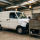 Camionetă albă de livrări în garaj comercial cu scule de mecanic, piese de schimb și facturi pe capotă.