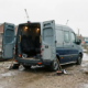 Dubbele cabine bedrijfsbus met open achterdeuren op Nederlandse bouwplaats, veiligheidsstoelen en gereedschap zichtbaar.