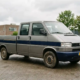 Camionnette d'occasion à double cabine, de couleur gris argenté, sur le parc d'un concessionnaire ; vue de trois quarts de face avec l'espace de chargement visible ; lumière du jour par temps nuageux.