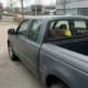 Camioneta gris oscuro de doble cabina en un parque empresarial holandés, con maletín de cuero y herramientas visibles a través de la ventanilla trasera.