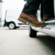 Chaussure de travail entrant dans le marchepied d'une camionnette blanche sur le parvis d'un concessionnaire en béton, angle de caméra bas avec mise au point nette.